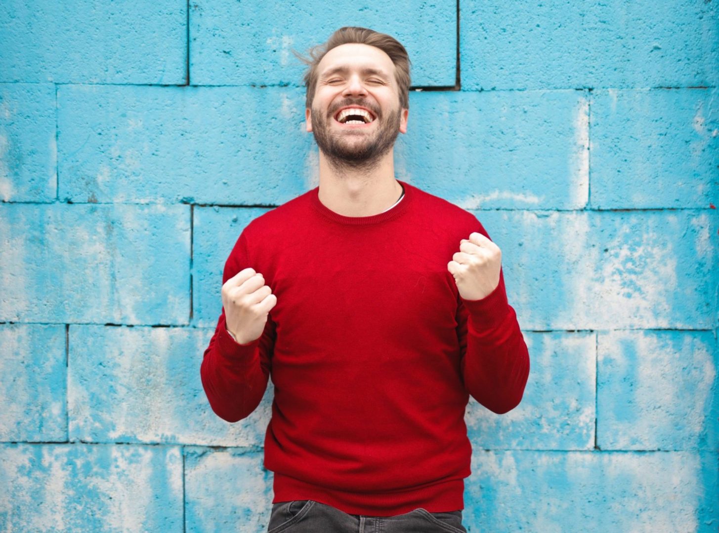 man wearing red long-sleeved shirt standing beside wall